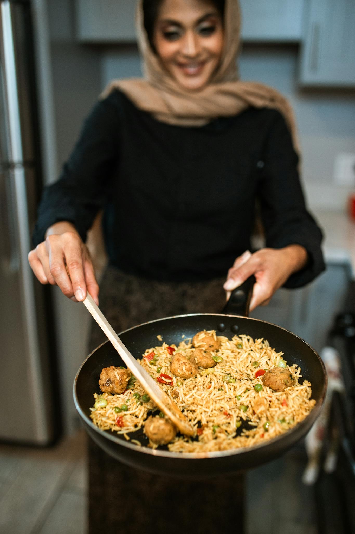 A woman in a hijab prepares a flavorful rice and meatball dish at home, showcasing culinary tradition.