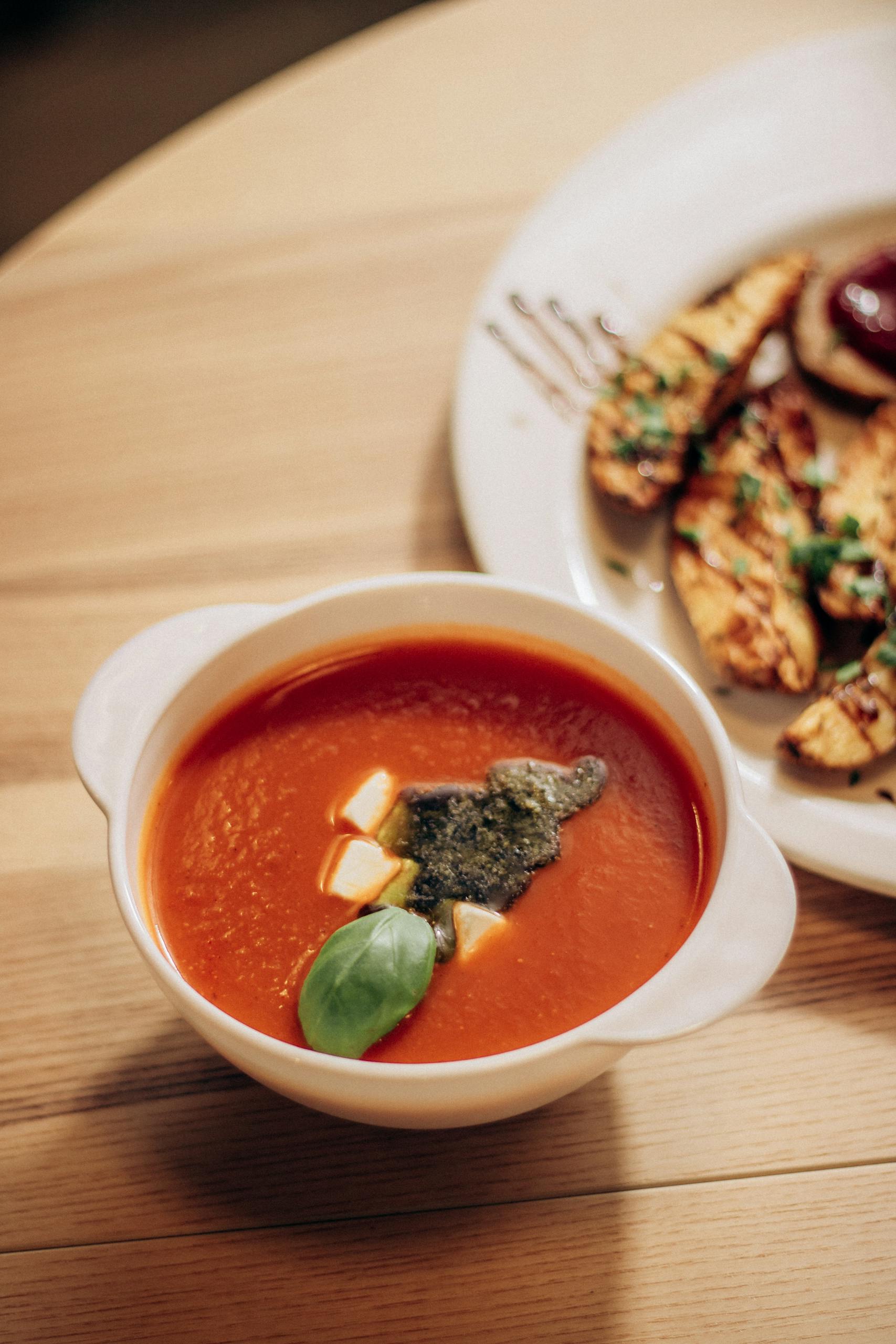 creamy tomato basil soup in a white bowl with fresh basil