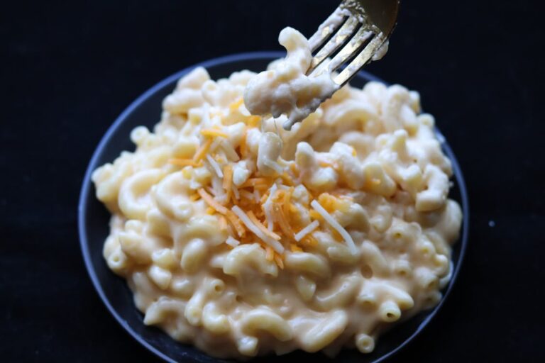 A bowl of creamy spicy mac and cheese topped with freshly grated cheddar, served on a dark background